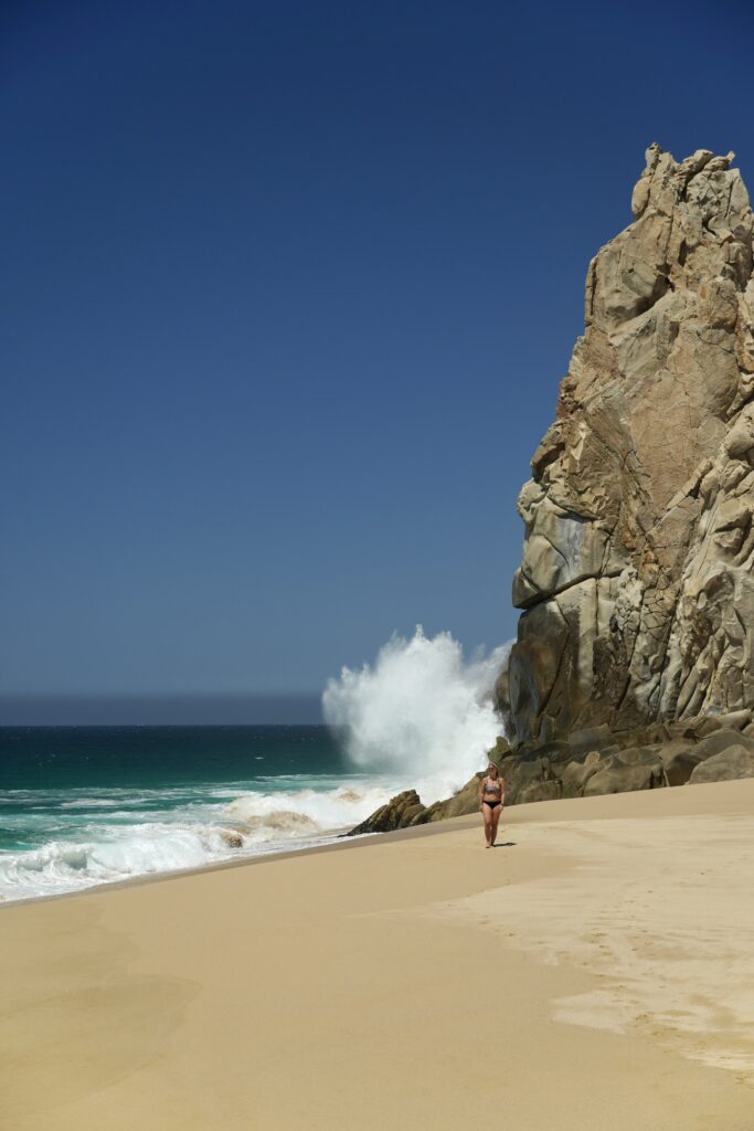 waves crashing along the rock cliffs at Divorce Beach with emily walking toward the camera