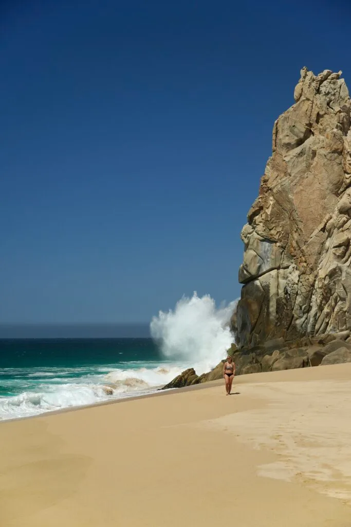waves crashing along the rock cliffs at Divorce Beach with emily walking toward the camera