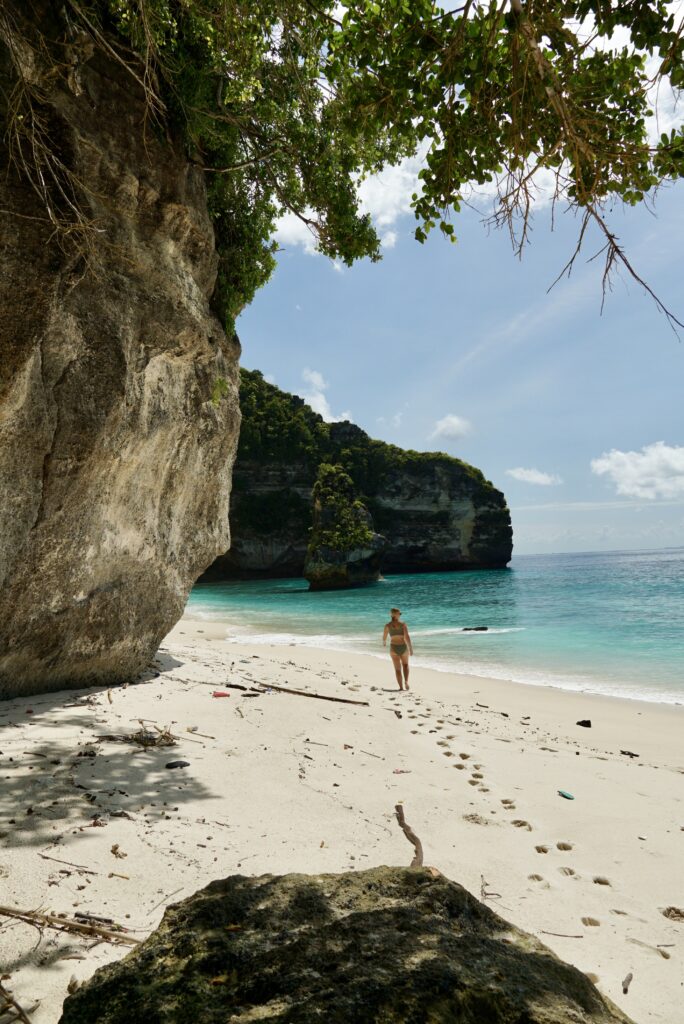 Emily walking in the sand toward the diamond shaped rock at the base of Suwehan Beach in Nusa Penida