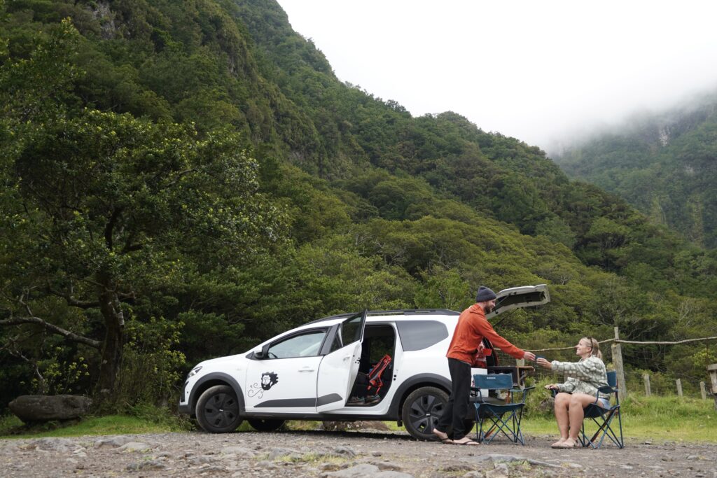 Jake handing Em a coffee cup sitting outside their Vanscape Rental